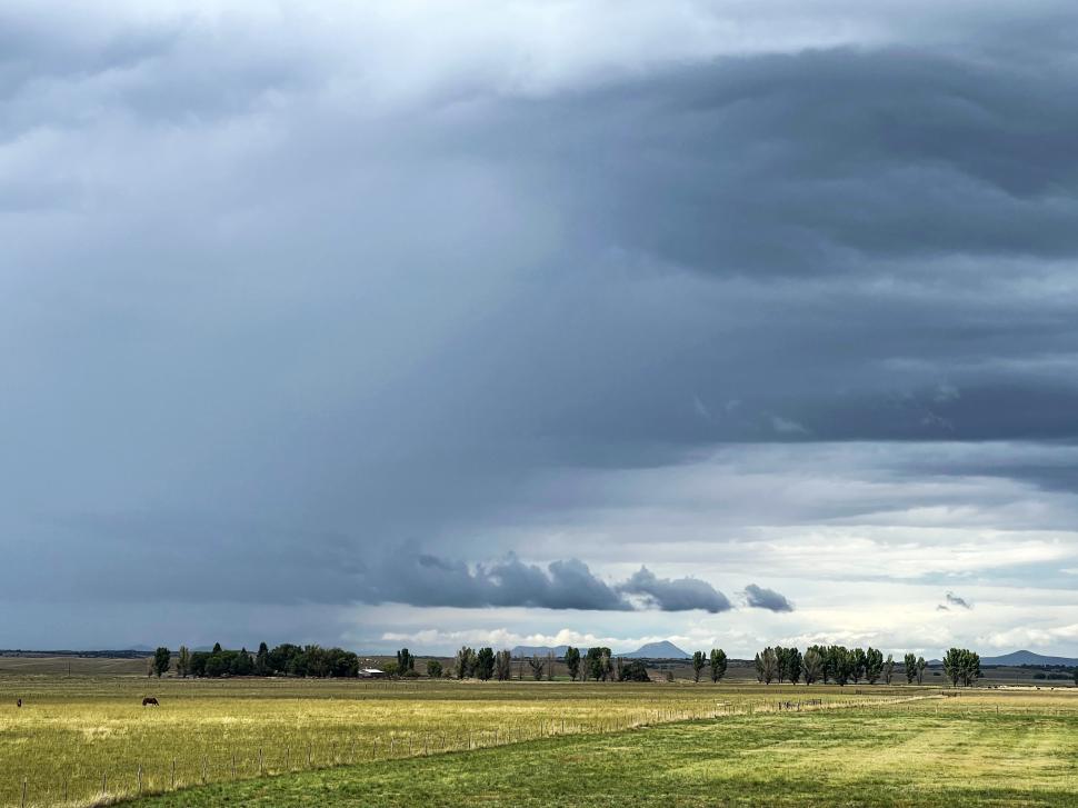 Free Image of Majestic clouds loom over a green field with distant mountains under gray skies 