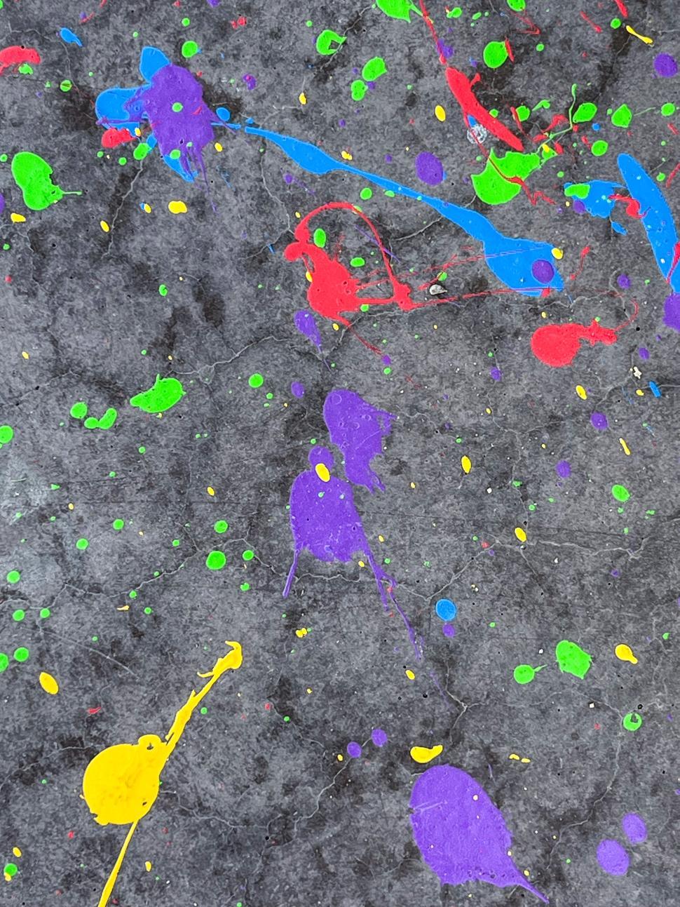 Free Image of Bright splashes of paint on a textured, dark surface create a colorful art scene 