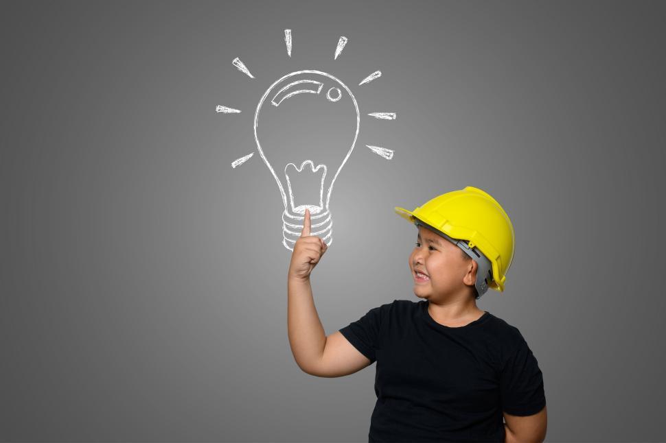 Free Image of A boy wearing a yellow engineer hat and a house plan on a blackboard 