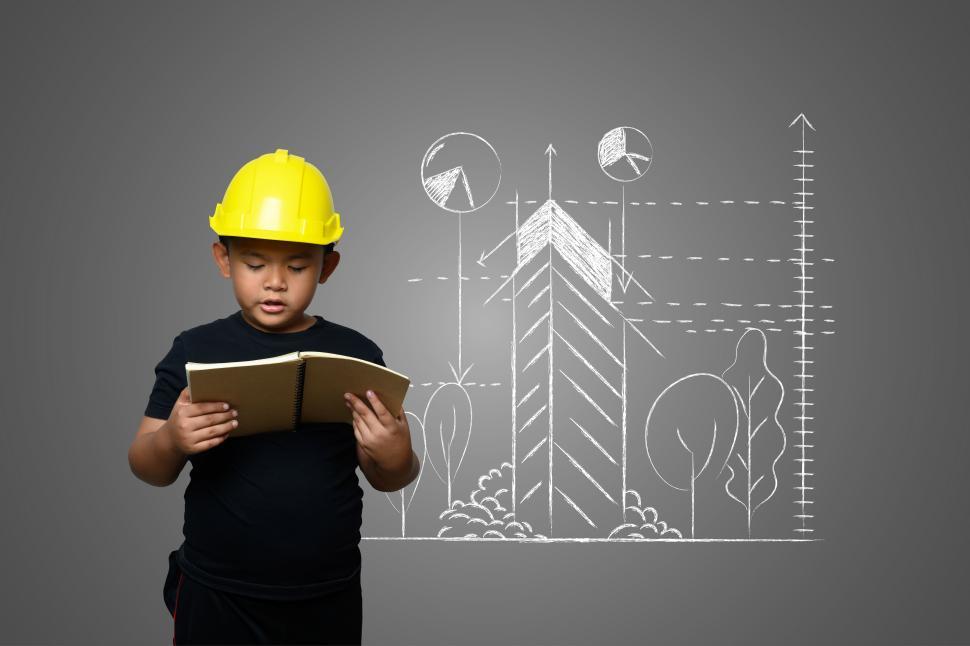 Free Image of A boy wearing a yellow engineer hat and a house plan on a blackboard 