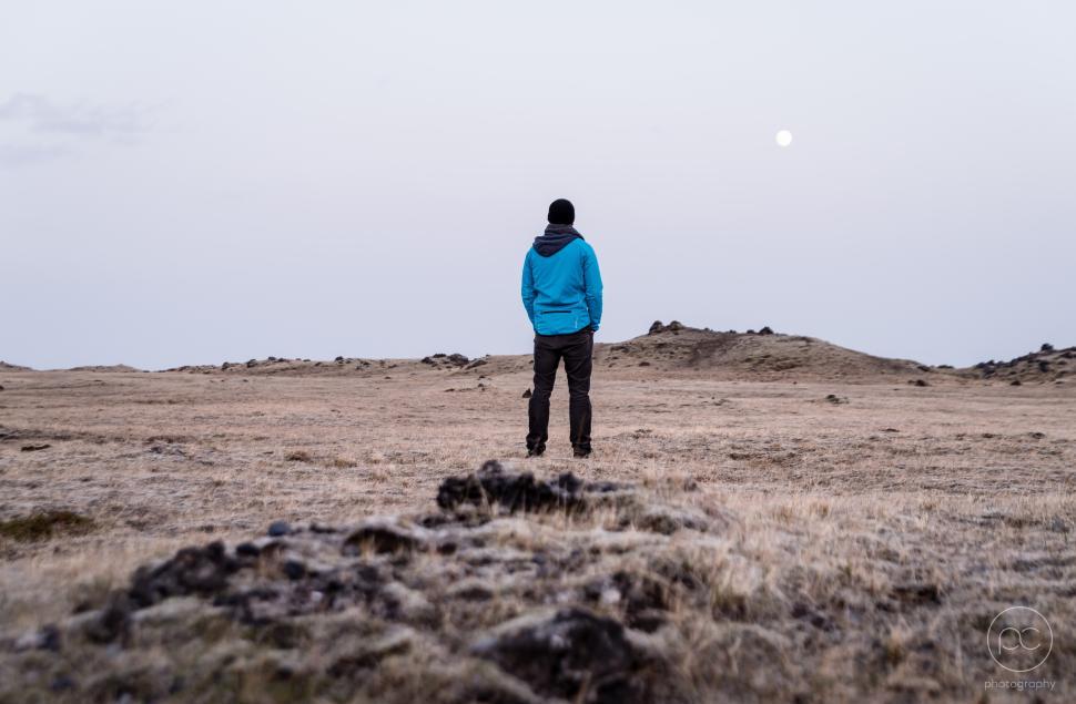 Free Image of Man gazes at the moon over a barren landscape at dusk 