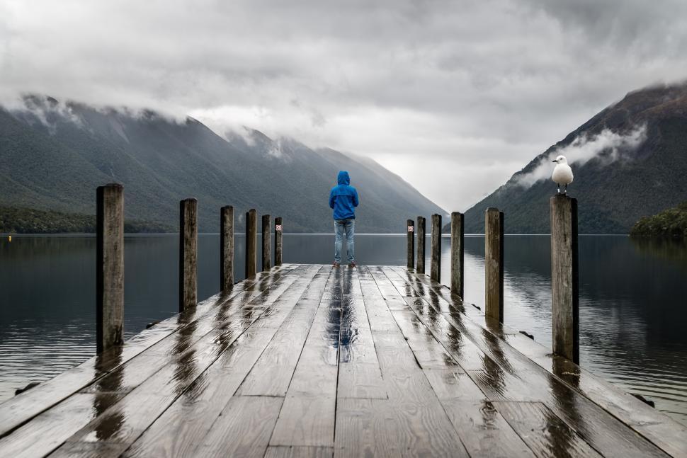 Free Image of Person stands on wet dock overlooking mountains and lake 