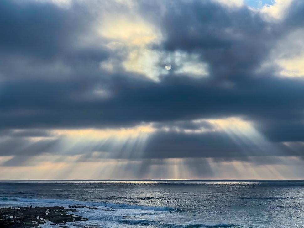 Free Image of Sunlight breaks through clouds over calm ocean waters at dusk 