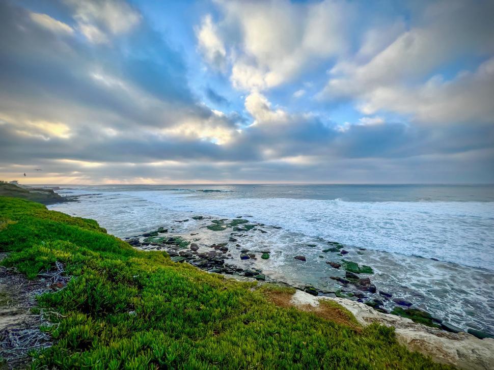 Free Image of Coastal view of waves crashing on rocks under a cloudy sky in San Diego, California 