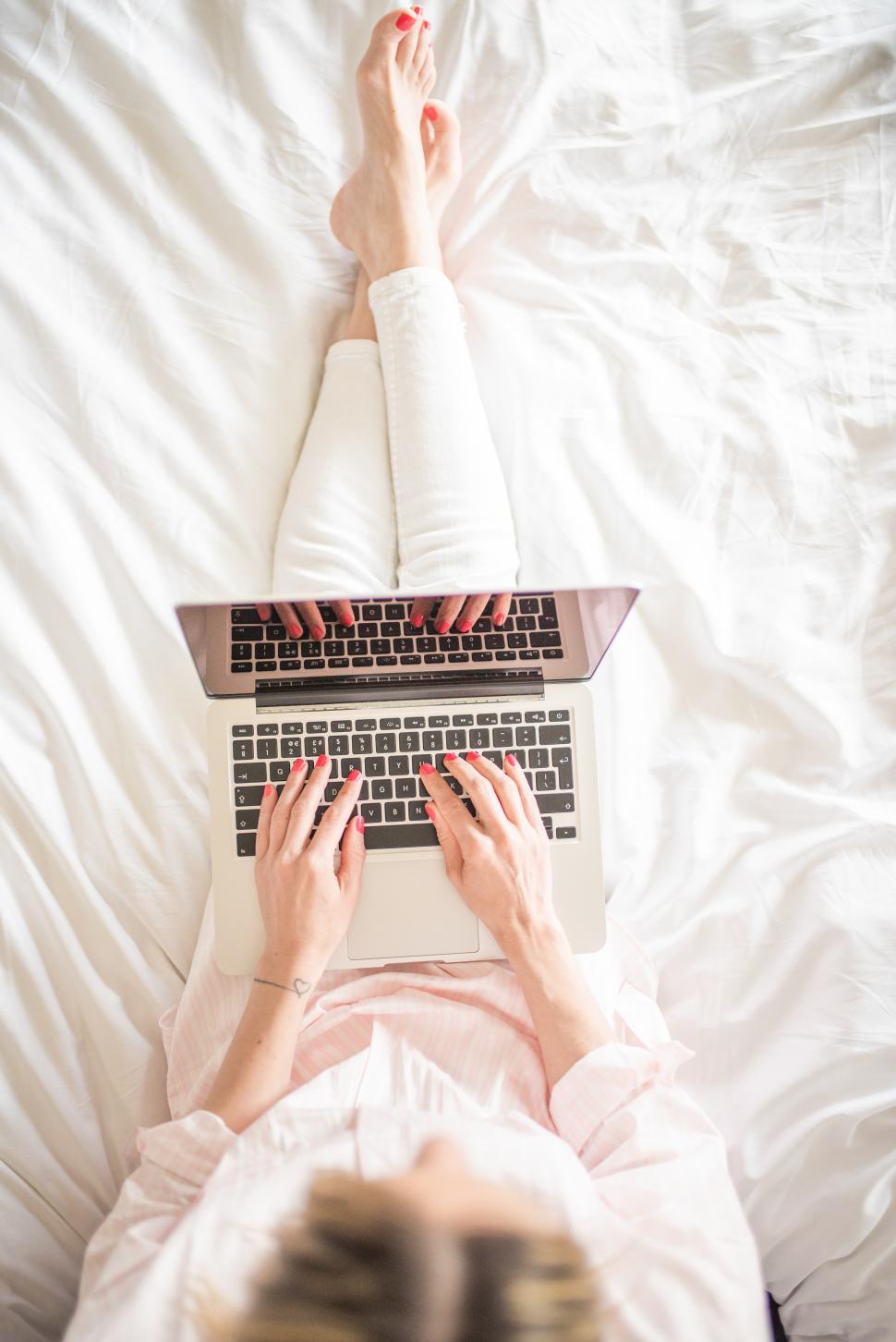 Free Image of Woman typing on laptop while sitting on bed during morning 
