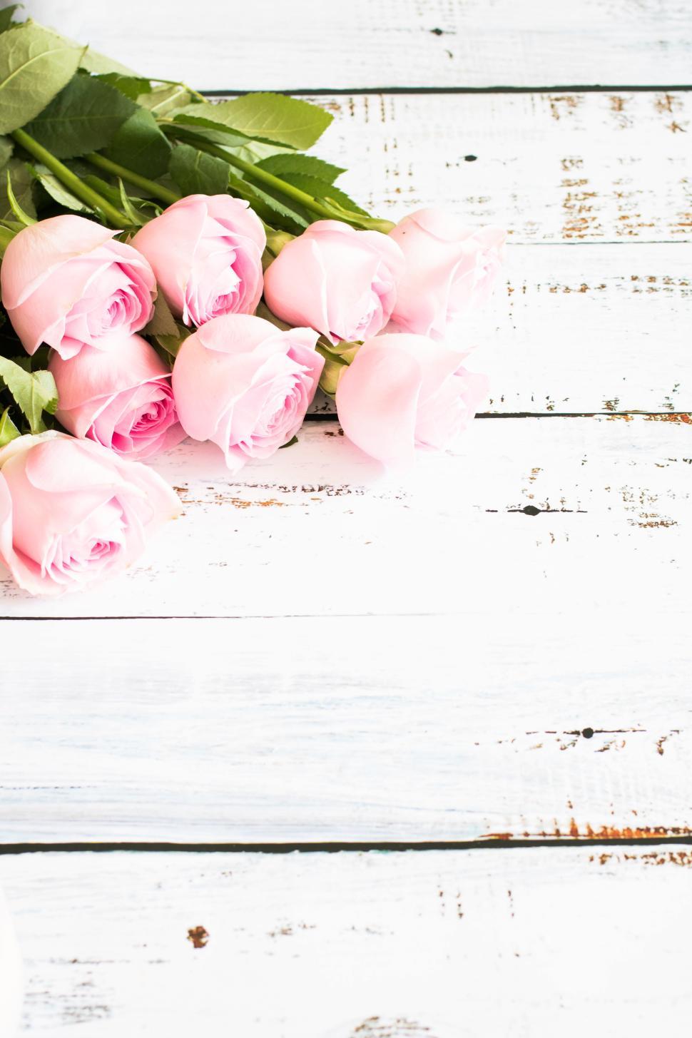 Free Image of Pink roses arranged on rustic wooden table surface 