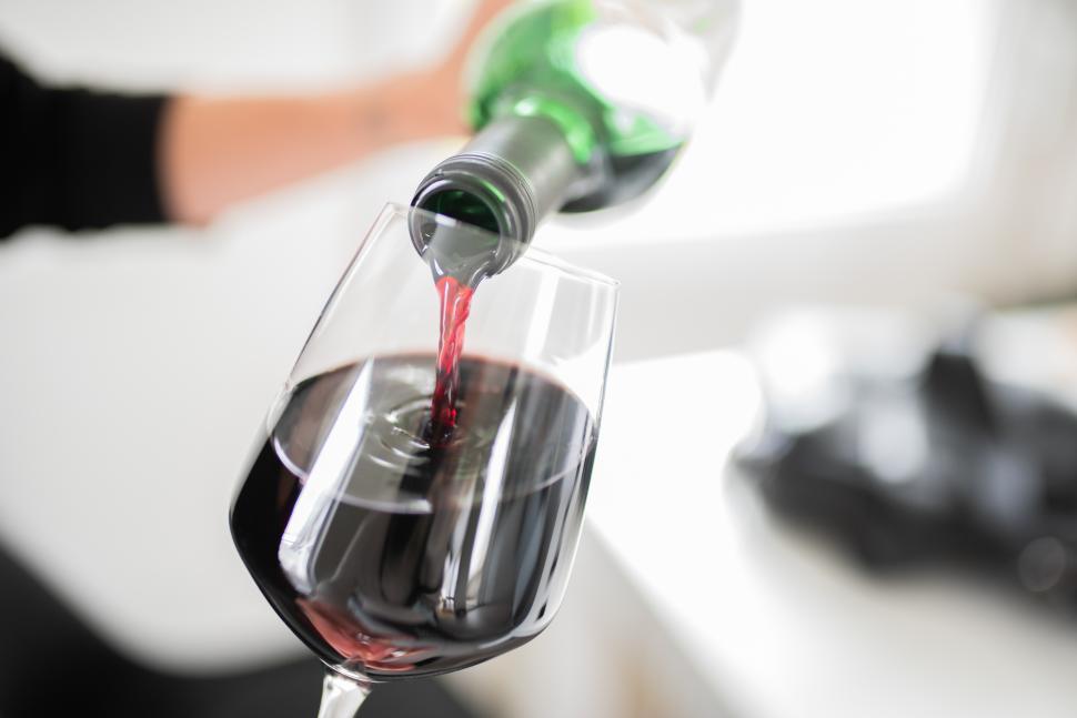 Free Image of Pouring red wine into a glass at a cozy setting 
