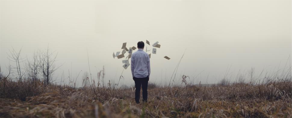 Free Image of Individual stands in a field surrounded by floating papers on a foggy day 