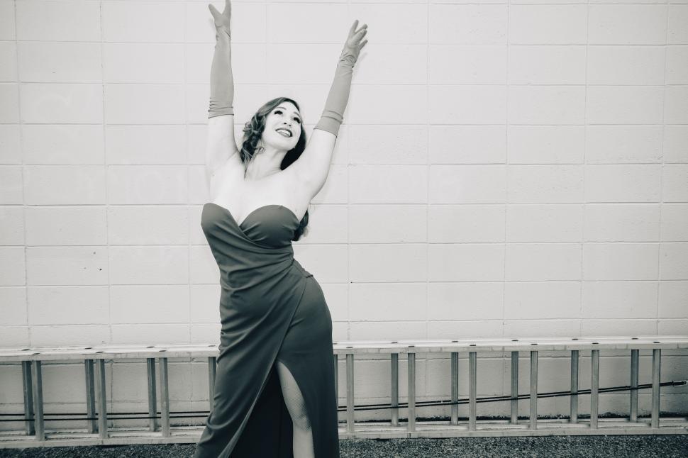 Free Image of Elegant woman in glamorous dress poses joyfully against a white wall 