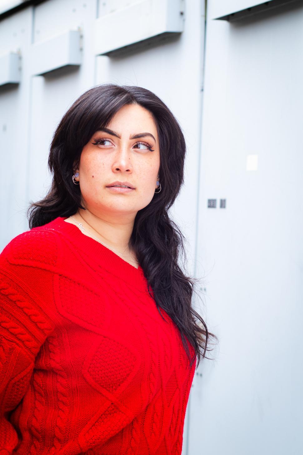 Free Image of Young woman in red sweater standing against metal background outside 