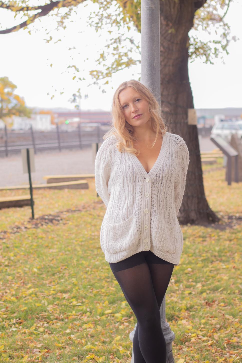 Free Image of Young woman stands gracefully by a lamppost in a park on a fall day 