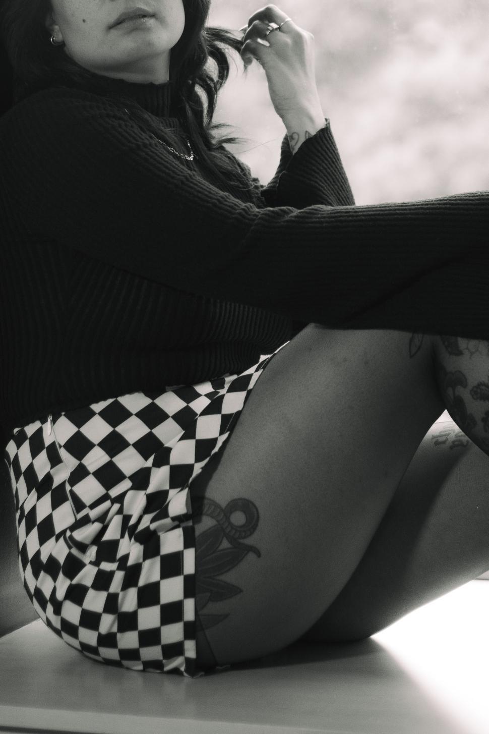 Free Image of Captivating portrait of a woman in checkered skirt and sweater by the window 
