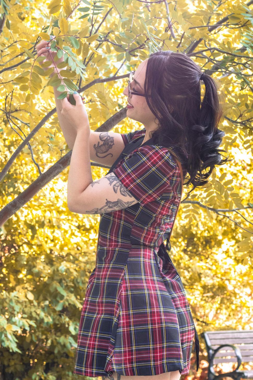 Free Image of Woman in plaid dress enjoys nature while picking leaves in autumn sunlight 