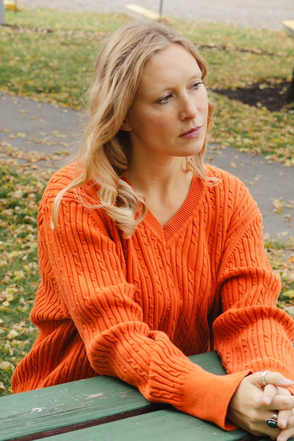 Free Image of Woman in orange sweater looks thoughtfully outdoors in autumn setting 