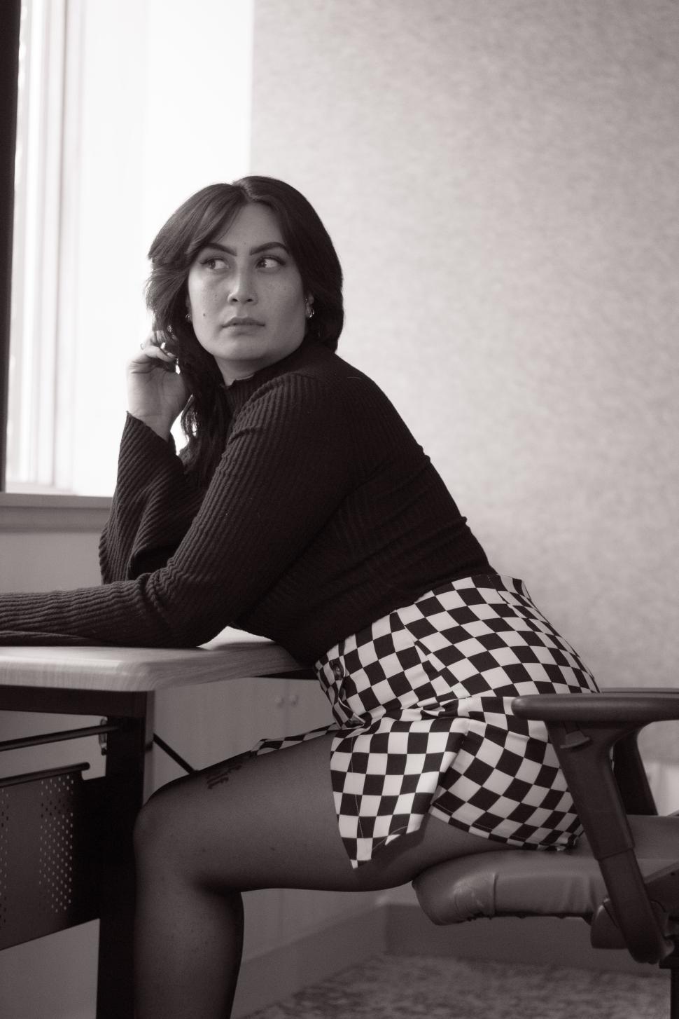 Free Image of Woman in a checkered skirt sitting at a desk in an office setting during daylight 