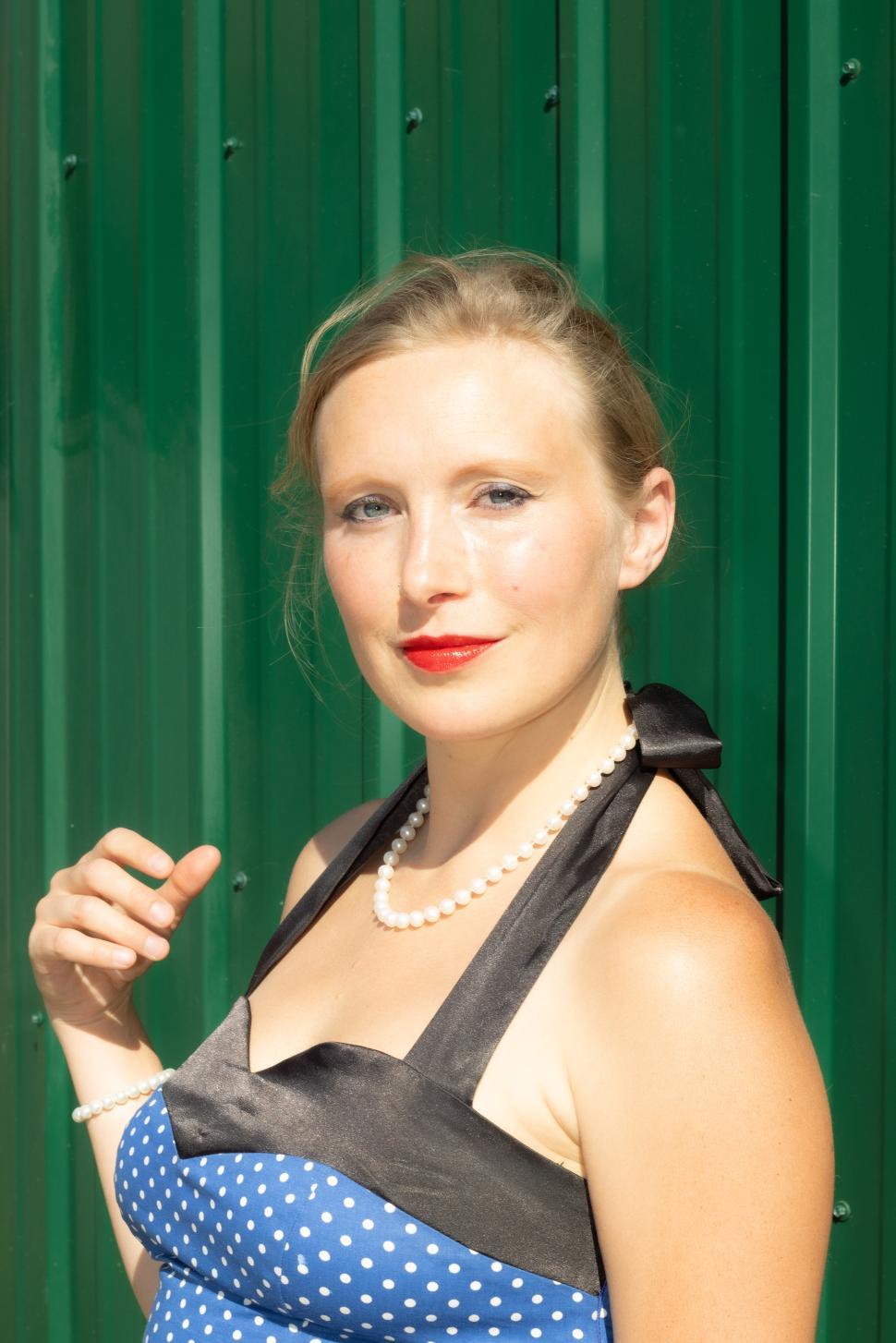 Free Image of Vintage style model poses elegantly against a green background in midday sunlight 