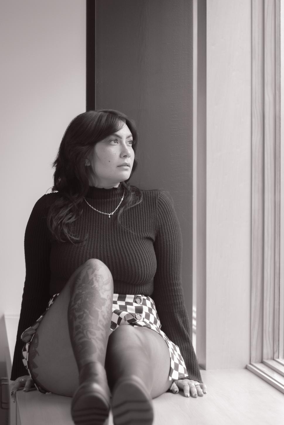 Free Image of Stylish woman sits by window, deep in thought 