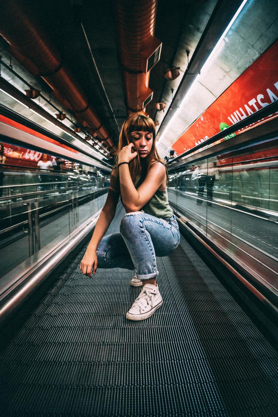 Free Image of Young woman crouching on moving walkway in urban setting 