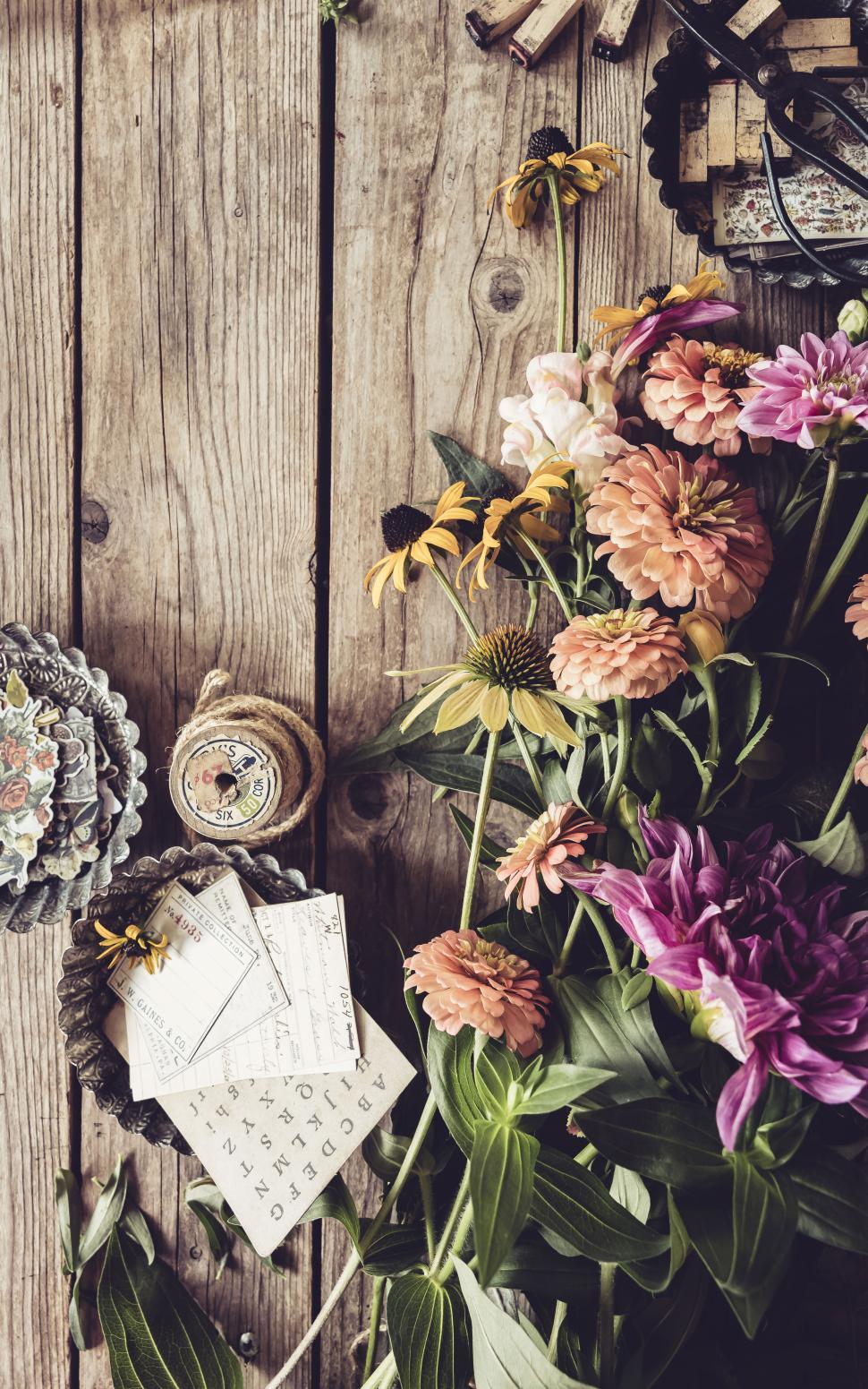 Free Image of Colorful flowers on a rustic wooden table with stationery supplies 