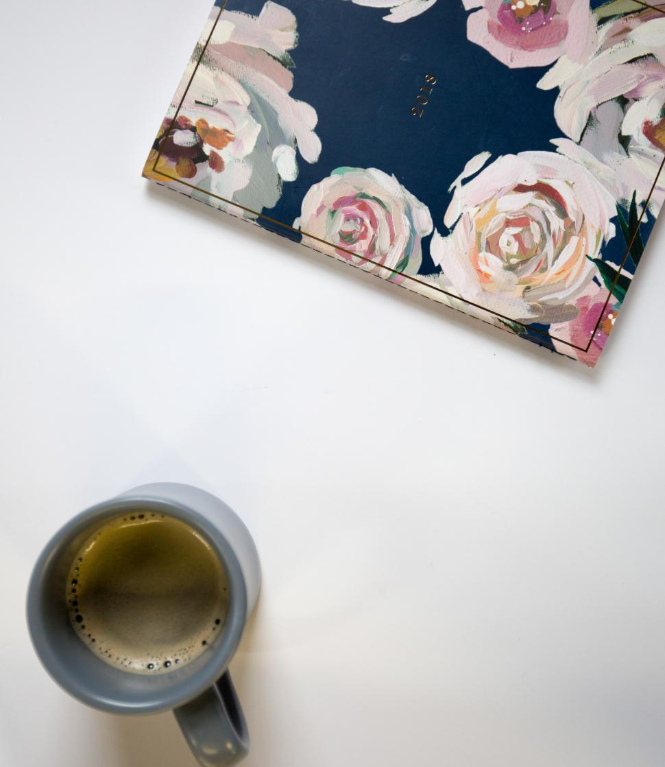 Free Image of Cozy morning setup with coffee and floral notebook on white table 