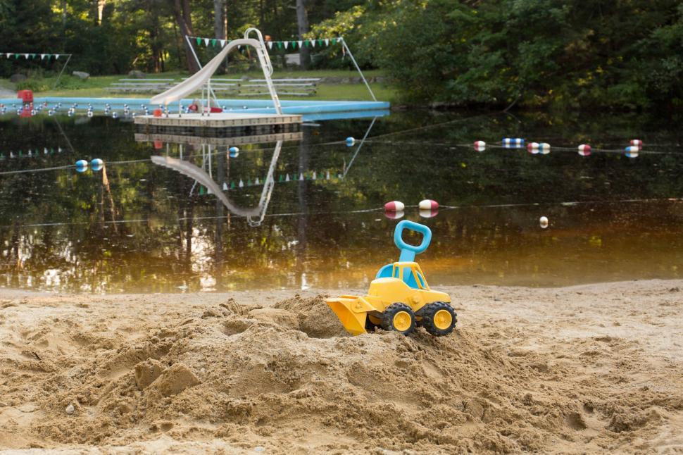 Free Image of Yellow toy truck on sandy beach near swimming area 