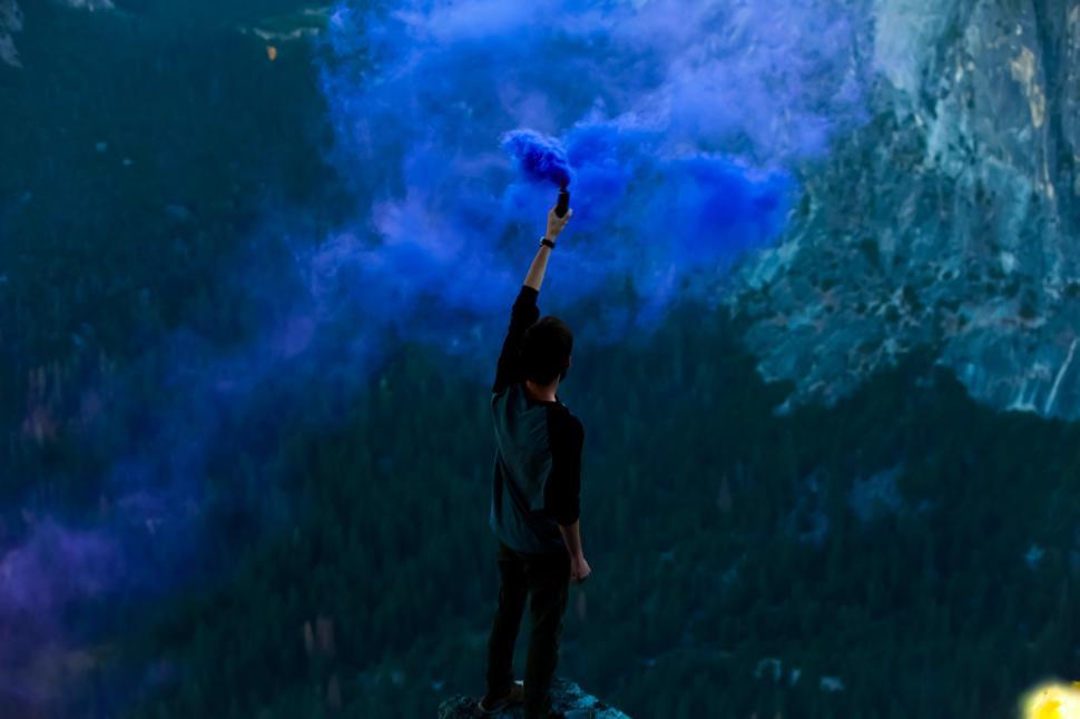 Free Image of Person holds blue smoke grenade at mountain edge 