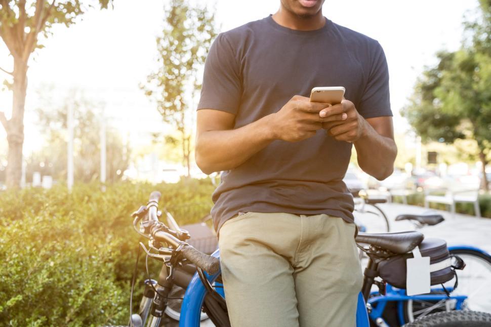 Free Image of Man using smartphone while leaning on bicycles outdoors 
