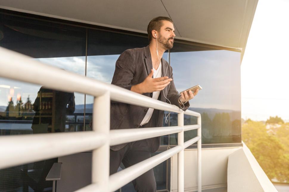 Free Image of Man enjoying music while standing on balcony at sunset 