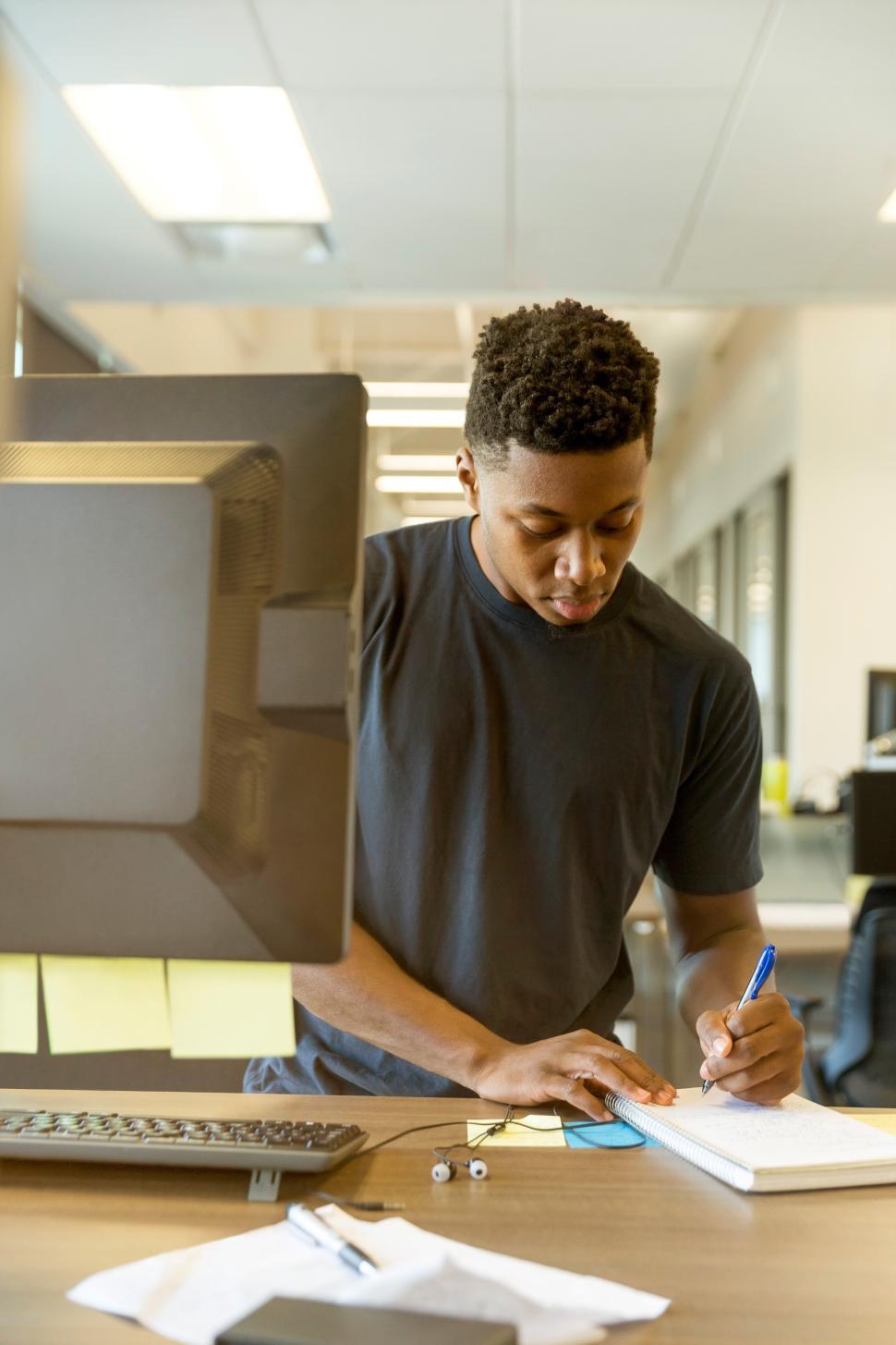 Free Image of Man writing notes at desk in modern office setting 