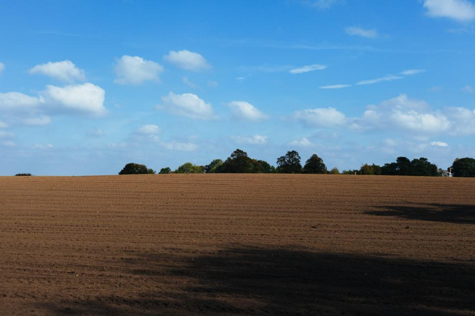 Free Image of Expansive farmland under a blue sky with fluffy clouds 