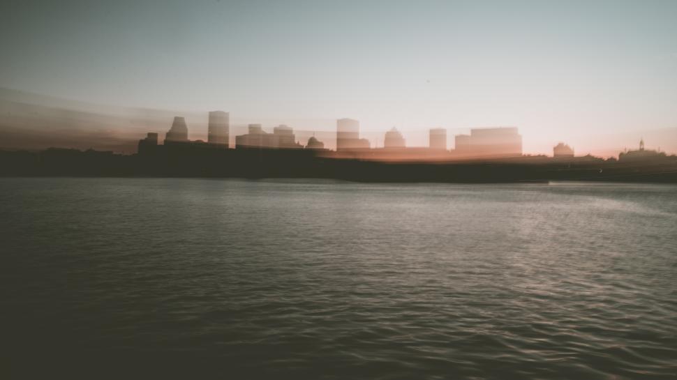 Free Image of Urban skyline at dusk reflecting on the calm river surface during sunset 