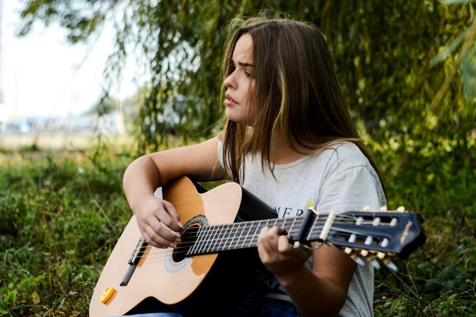 Free Image of Young woman playing guitar outdoors in natural setting 
