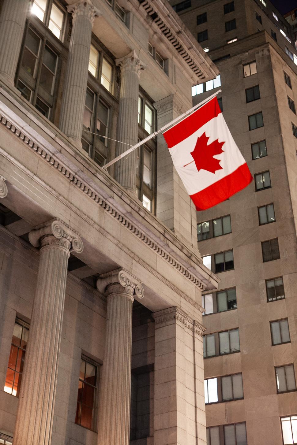 Free Image of Canadian flag waving near historic building at night in urban setting 