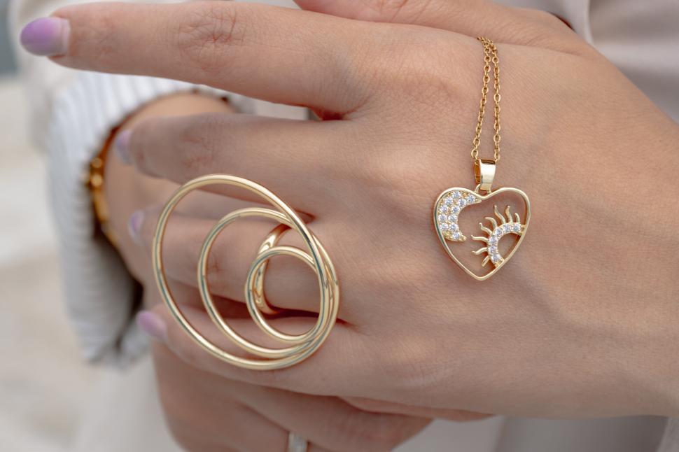 Free Image of Woman's hand with golden jewelry and heart necklace  