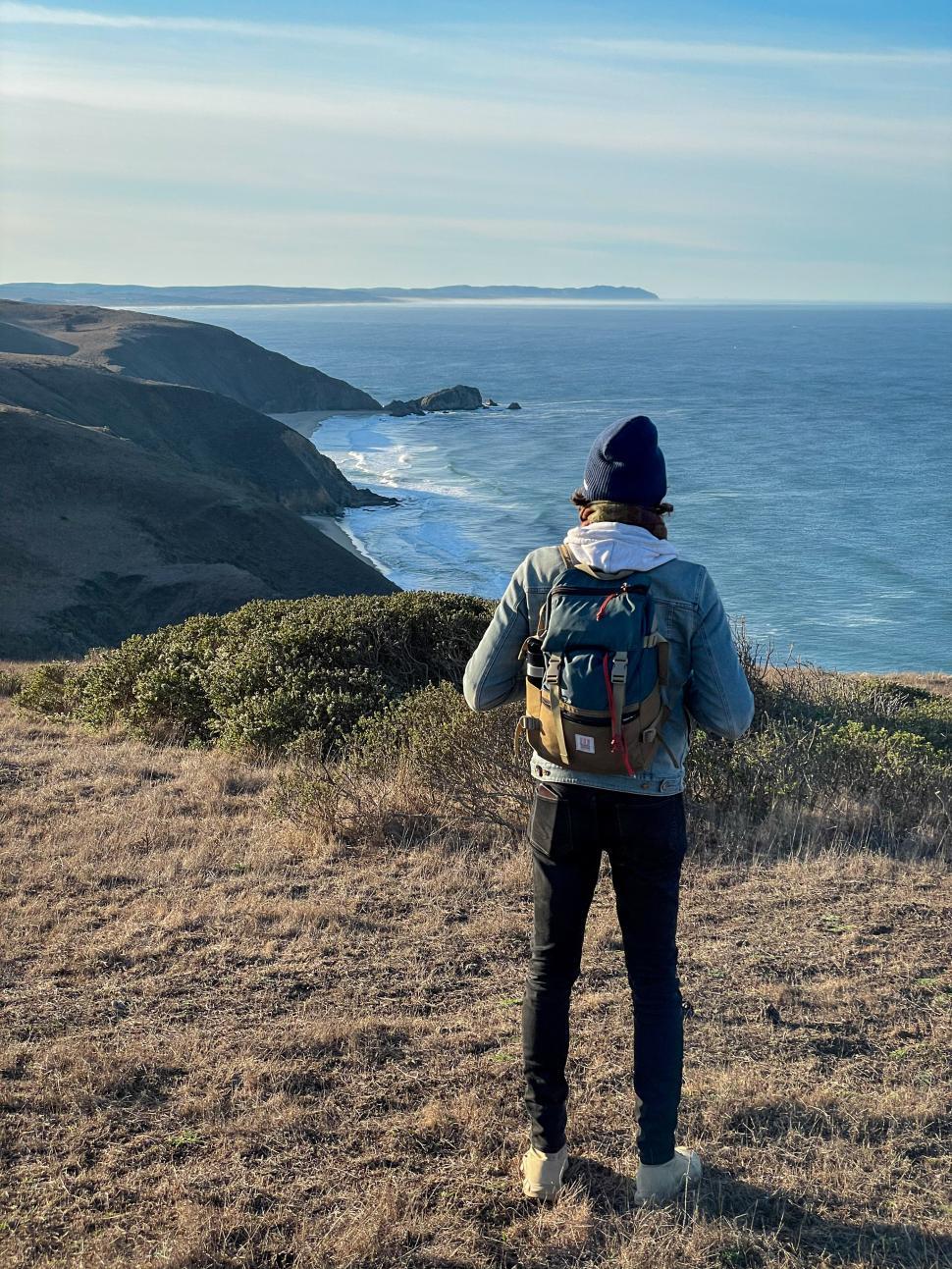 Free Image of Adventurer stands on cliff overlooking ocean at sunset 