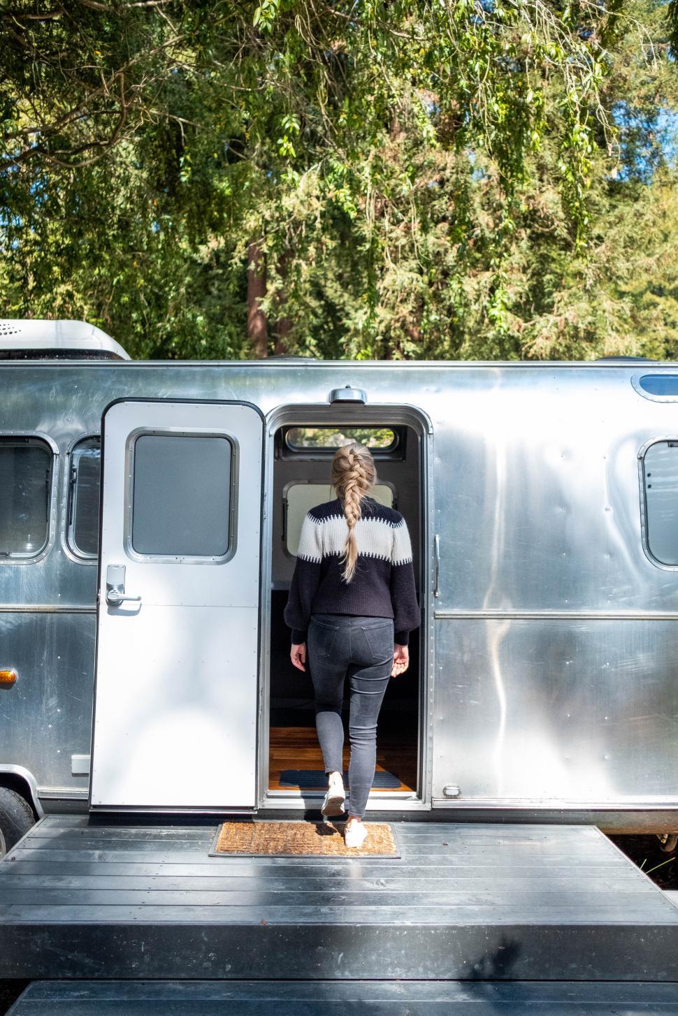 Free Image of Woman entering a vintage trailer in a serene forest setting 