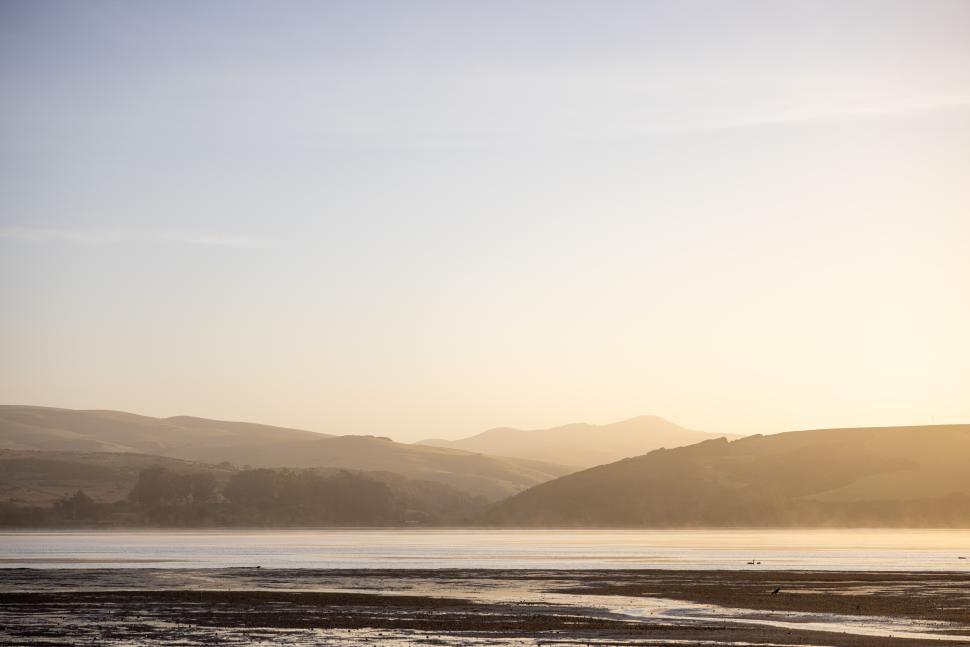 Free Image of Golden sunrise lights up the serene landscape with distant mountains and calm water 