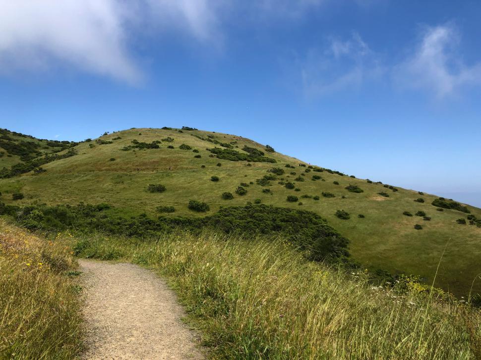 Free Image of Hiking trail on a sunny day near rolling green hills 