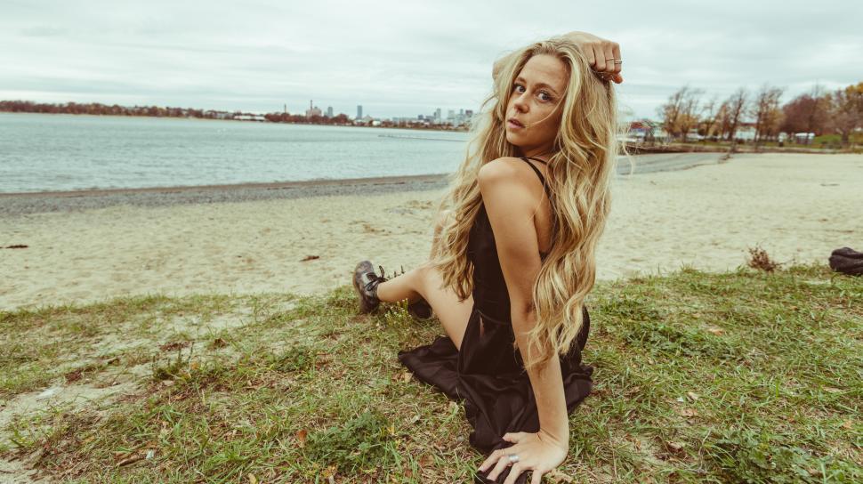 Free Image of Woman in black dress sitting on the grass by the water s edge 