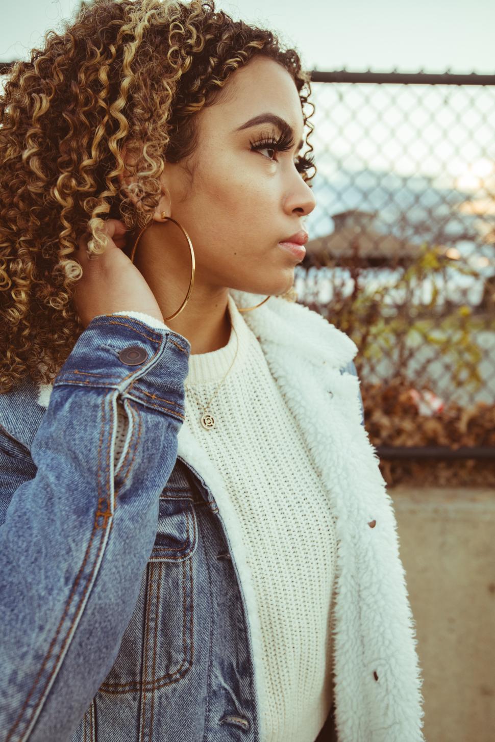 Free Image of Woman posing outdoors near a fence at sunset 