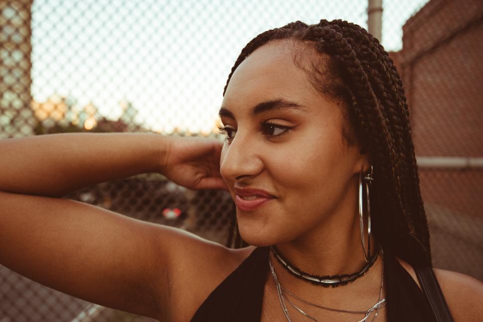 Free Image of Young woman poses confidently by a chain-link fence at sunset 