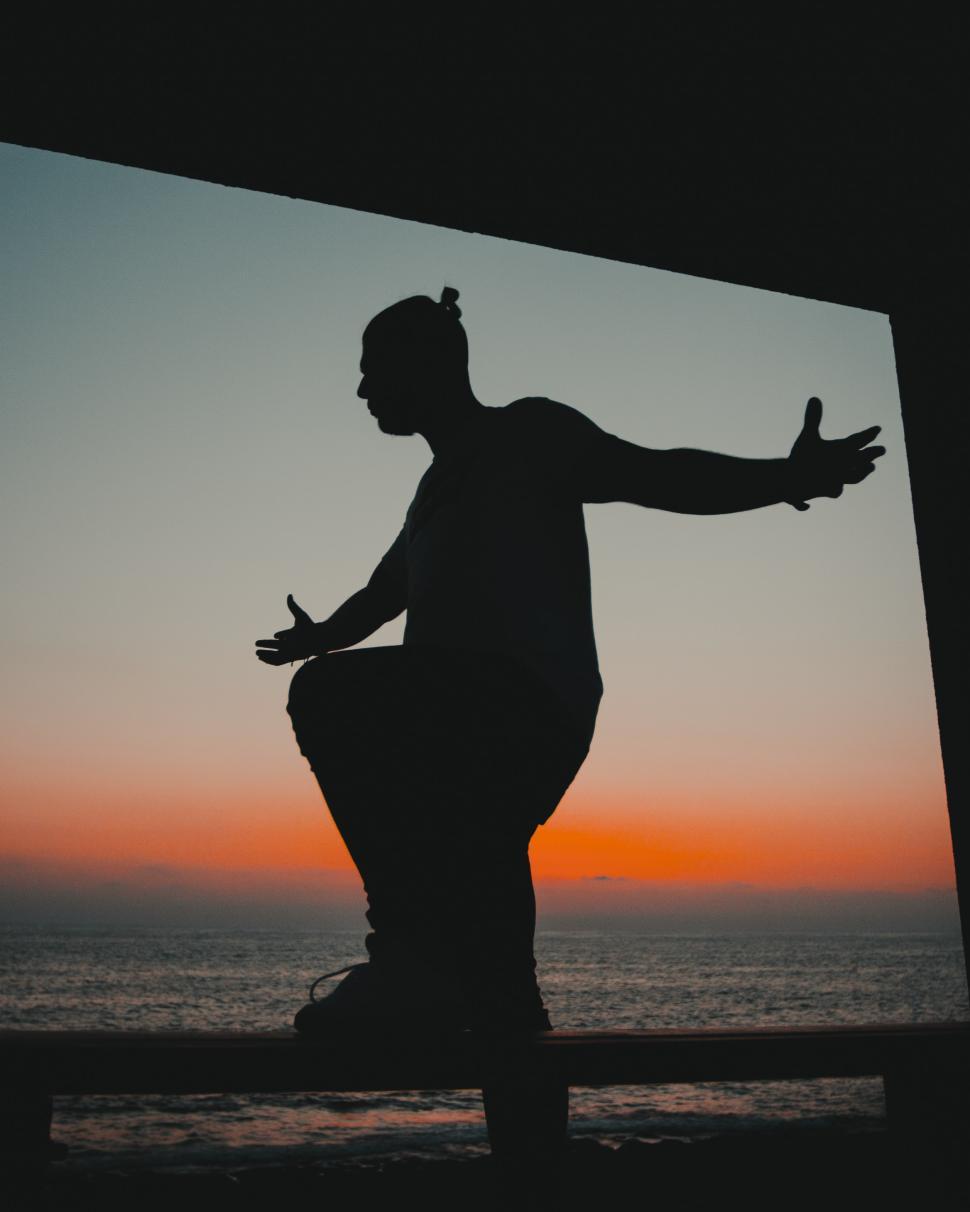 Free Image of Silhouette of a person against a vibrant sunset by the sea 