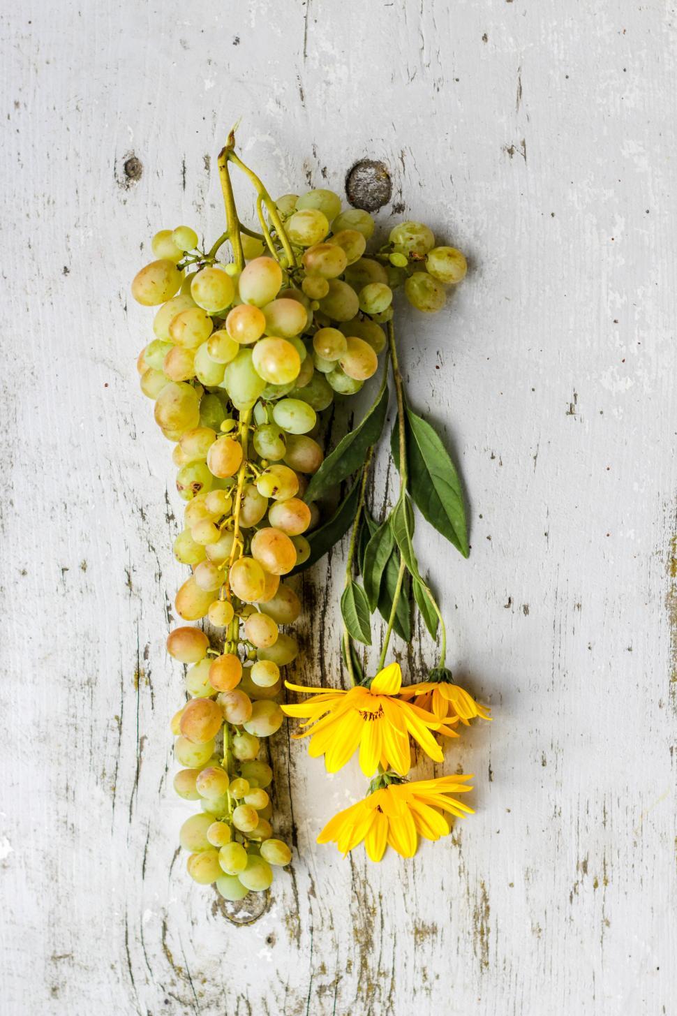 Free Image of Fresh green grapes and vibrant yellow flowers on wood 