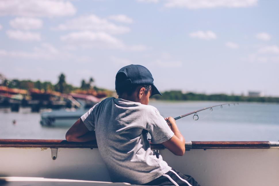 Free Image of Child enjoys fishing from a boat on a sunny day by the water 