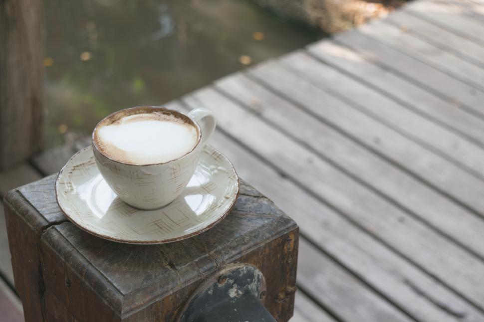 Free Image of Warm cup of coffee sits on wooden post by serene water edge during morning hours 