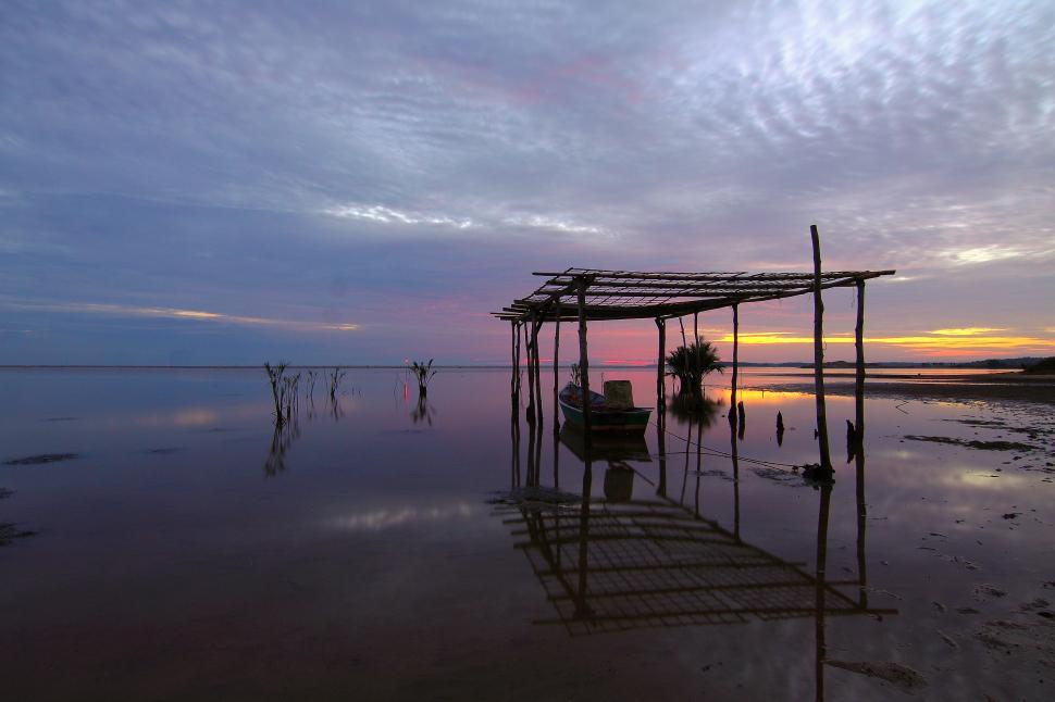 Free Image of Sunset reflections over calm water with wooden structure 