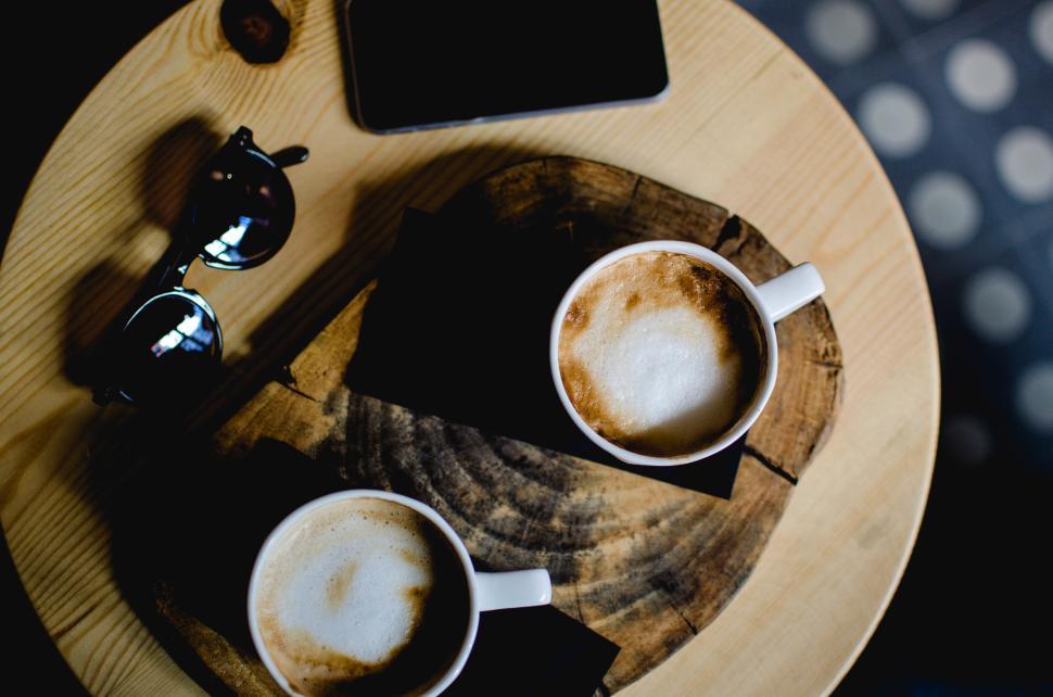 Free Image of Coffee cups on a wooden table with sunglasses and a device in a cafe 