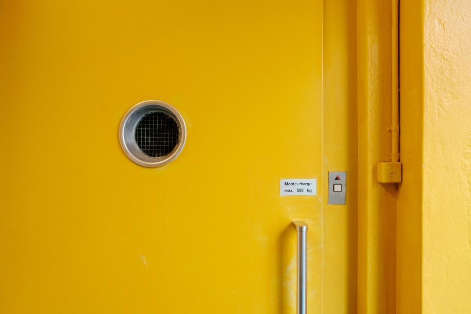 Free Image of Bright yellow door with circular window and control panel in modern building 
