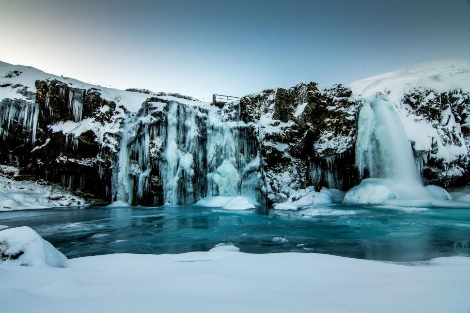 Free Image of Winter landscape featuring a frozen waterfall and icy river in a peaceful setting 
