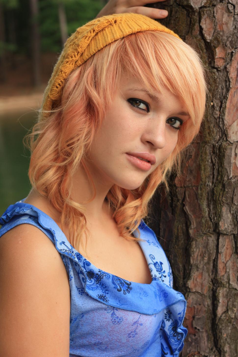 Free Image of A beautiful young woman posing against a tree by a lake 